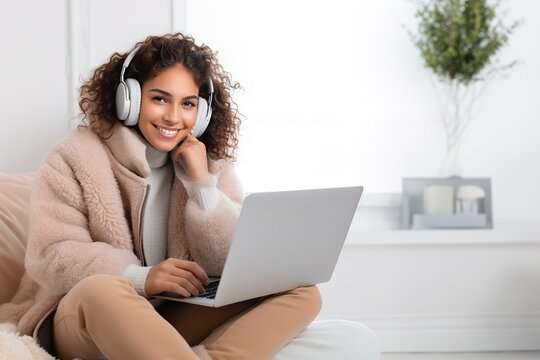 Beautiful Latina Woman Sitting In The Couch Using Laptop And Headphones During Cozy Winter At Home