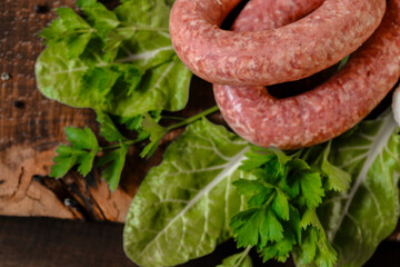 sausages in rustic style.Raw sausage rings, fresh parsley, on lettuce leaves on a wooden...