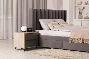 Stylish bedroom in soft light colors with comfortable bed and bedside table. Interior design