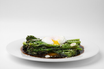 Tasty cooked broccolini with poached egg, almonds and sauce on white background, closeup