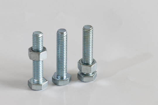 conjunto de tres pernos o tornillos con tuercas met&aacute;licas sobre superficie color gris