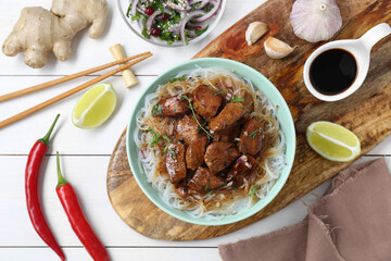 Bowl with pieces of soy sauce chicken and noodle on white wooden table, flat lay
