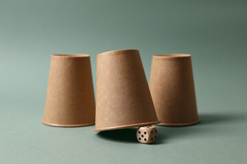 Three paper cups and dice on pale olive background. Thimblerig game