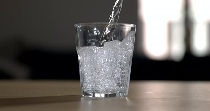 Pouring sprinkling water into glass cup in super slow-motion 800 fps. Serving hydrating drink