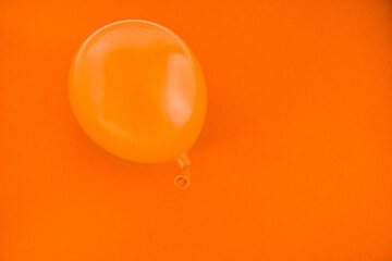 Einzelner orangefarbener aufgeblasener Luftballon vor orangefarbenem Hintergrund, horizontal 