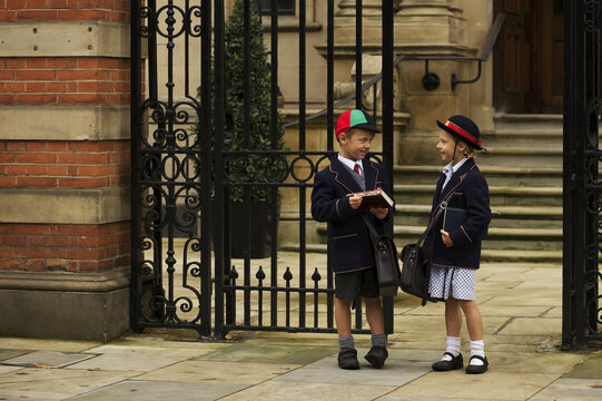 Young Boy And Girl Students In Uniform Talking Outside The School; London, England