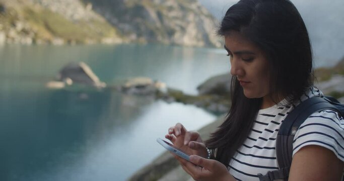 Young female trekker using her phone to check the maps by a mountain lake in the Swiss alps and smiling