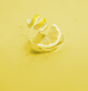 Lemon Wedge And Curled Peel Dropping Into Yellow Liquid; Toronto, Ontario, Canada