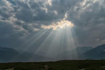 Sun filtering between the grey clouds creates dramatic beams of light during a smoky day in the Yukon; Yukon Territory, Canada
