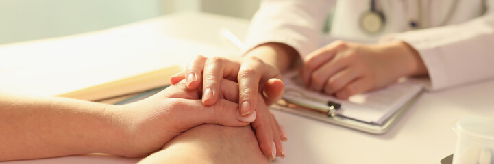 Doctor puts her hand on hands of patient, sitting with her in medical clinic.
