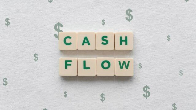 Green Dollar Signs Going Up Behind The Cash Flow Shown On Scrabble Blocks.