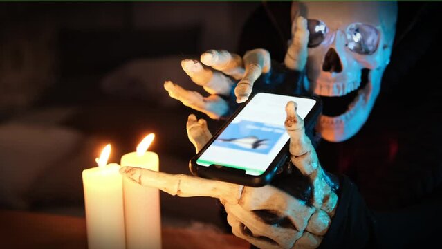 Close-up, screen smartphone watch mysterious character in skeleton costume in image of death, scrolls through feed on social network, examines photo in light candles. Halloween party invitation.
