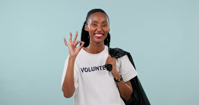 Cleaning trash bag, volunteer and black woman okay sign for garbage pollution project, community service or studio feedback. NGO opinion vote, ok emoji icon or portrait person wink on blue background