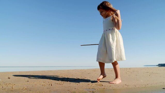 Girl child drawing with a stick on the sand on the beach and having fun