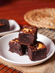 Chocolate pound cake. A piece of cake is cut into pieces and served with chocolate ganache cream. Brown wooden background. Dark mood.