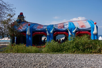 Sochi, Krasnodar region, Russia – August 5, 2023: Inflatable playroom by the sea. Pebbles, grass, tree, cloudy sky.