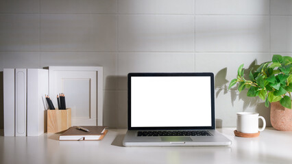 Laptop computer, coffee cup, potted plant and picture frame on creative workplace. Blank screen for your advertising text.