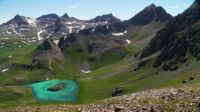 Aerial cinematic upper view  Ice Lake Basin Silverton Island Lake aqua blue clear water alpine tundra stunning mountain range snow wildflowers mid summer daytime beautiful slow pan to the left motion