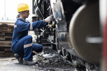 Male engineer maintenance locomotive engine, wearing safety uniform, helmet and gloves in locomotive repair garage. Male railway engineer repair train wheel in train garage