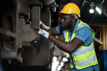 African American male engineer maintenance locomotive engine in locomotive repair garage. Male railway engineer use wrench repair train wheel in train garage