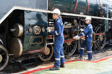 Male and female engineer maintenance locomotive engine, wearing safety uniform, helmet and gloves in locomotive repair garage. Male and female railway engineer repair train wheel in train garage