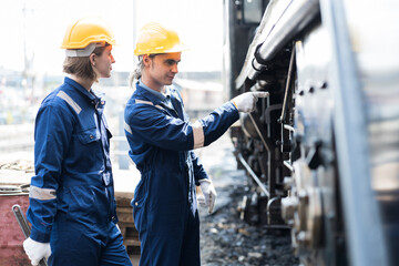 Male and female engineer maintenance locomotive engine, wearing safety uniform, helmet and gloves in locomotive repair garage. Male and female railway engineer repair train wheel in train garage