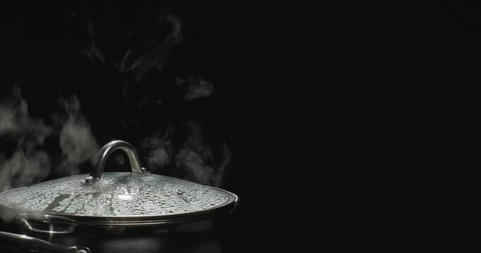 Pot and steam in the kitchen. Steam comes out of the saucepan while cooking. Boiling water in pan on black background. Slow motion