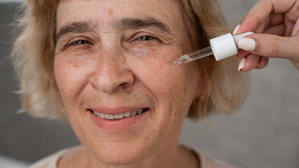 Close-up portrait of an old woman applying hyaluronic acid serum with a pipette. Anti-aging face...