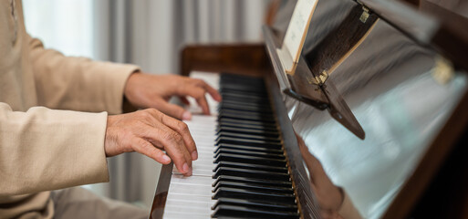 Asian senior retired man learning to play piano at home, Old man playing music on piano in living room at home, lifestyle life after retirement, fingers touching on keyboard