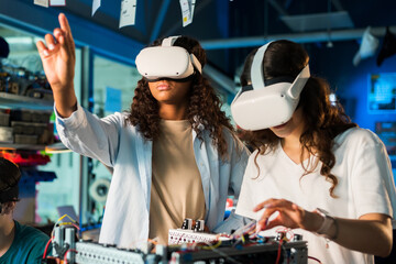 Two young women in VR glasses doing experiments in robotics in a laboratory