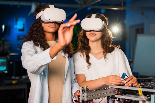 Two young women in VR glasses doing experiments in robotics in a laboratory