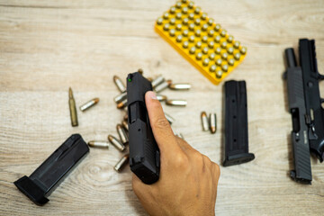 Male hand holding a pistol, bullets and mags on a wooden table.