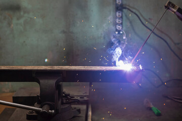 Caucasian Mature Professional Male Welder in Protective Mask During Welding Process of Metal Rod At Factory.