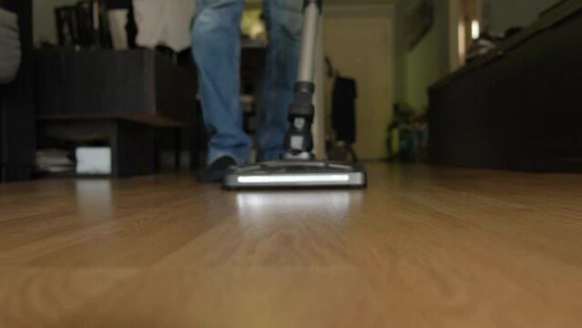 A cordless vacuum cleaner with a turbo brush and lighting cleans a laminate floor close-up.