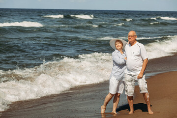 An elderly couple is standing on the beach by the sea.