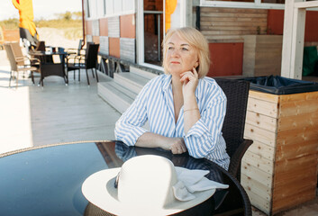 A lonely woman sits at a table in a cafe by the sea, looking at the waves.