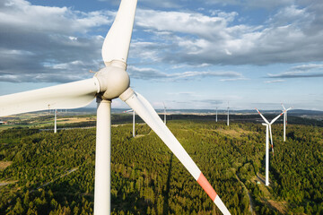 Wind turbines in a hilly forest in front of a partly cloudy, but sunny sky are seen from an aerial...