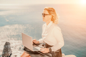 Business woman on nature in white shirt and black skirt. She works with an iPad in the open air with a beautiful view of the sea. The concept of remote work.