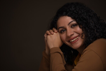 Adult woman with leaning head on both hands looking at camera and smiling 