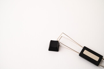 A close-up of a detached mechanical keyboard keycap placed near a stainless steal keycap and switch puller tool on a white background. Copy space.
