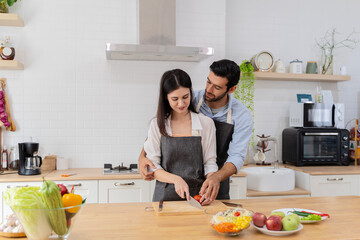 In the kitchen, a happy couple perfectly prepares healthy food, lots of vegetables, a guy juggles with fruits, making her boyfriend laugh.