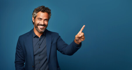 A handsome middle-aged man, isolated on an empty blue background, with a smile, positive and confident expression, pointing his finger to the side, showing an idea, a concept, a success - obrazy, fototapety, plakaty