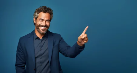 Foto op Aluminium A handsome middle-aged man, isolated on an empty blue background, with a smile, positive and confident expression, pointing his finger to the side, showing an idea, a concept, a success © mozZz