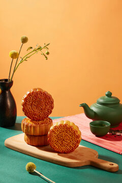 Wooden chopping board featured several baked mooncakes. Green tea set is decorated with black flower pot. Concept MoonCake on Mid Autumn Festival