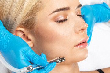 The cosmetologist makes the procedure Microdermabrasion of the facial skin of a beautiful, young woman in a beauty salon.Cosmetology and professional skin care.