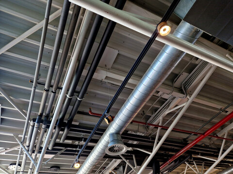 the air handling unit is on the ceiling of the building and is visibly left uncovered. the lights and pipes running under the tin roof give it an industrial feel. whire