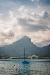 Boat with sails down floating on water surface of Lake Wolfgangsee in Austria. Alps mountain and cloud sky