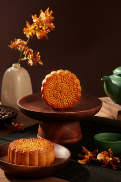 Delicious Chinese traditional mooncakes displayed on wooden dishes. Green tea set arranged behind with a flower pot. A time of year that the moon is at its brightest