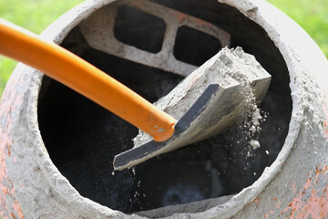 Construction site. Adding lime, sand and stones to rotating cement mixer. Builder working with...