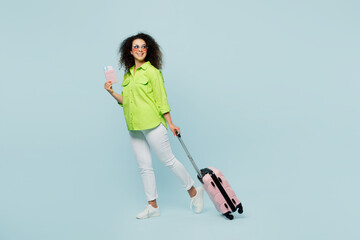 Traveler latin woman wear green casual clothes hold bag passport ticket look aside isolated on plain blue background. Tourist travel abroad in free time rest getaway. Air flight trip journey concept.